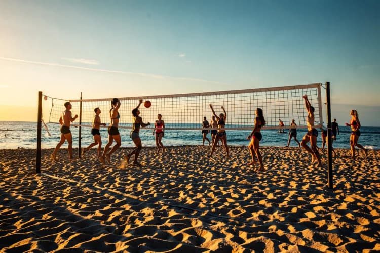 Grupo de pessoas praticando esportes em uma quadra de areia na praia.