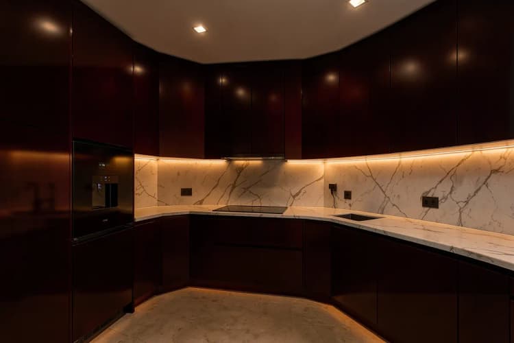 Cozinha de apartamento com armários planejados em tons escuros, bancada de mármore e eletrodomésticos embutidos.